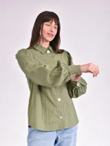 Camisa verde con rayas verticales, cuello clásico, cierre con botones y mangas largas abullonadas.