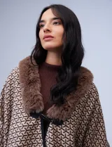 Ruana de tejido suave, color beige y marrón con estampado geométrico repetitivo. Posee cuello con aplique de piel sintética marrón y ribetes negros. Se combina con un suéter marrón de manga larga con botones en el puño.