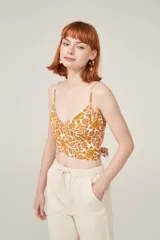 Top sin mangas con estampado floral en tonos amarillos y naranja, con diseño ajustado y detalles de lazo.