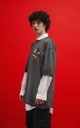 Remera oversize de algodón premium, color gris oscuro con efecto gastado (acid wash), con cuello redondo y manga corta. Presenta un pequeño estampado de Mickey Mouse en el pecho.