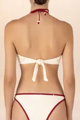 Top de bikini bandeau blanco marfil con ribete rojo oscuro. Tiene tiras que se anudan al cuello para un amarre halter, adornadas con delicados detalles de cuentas doradas.