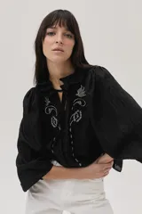 Blusa blanca con lunares en relieve, cuello con volados y lazos, mangas abullonadas 3/4 y bordados con lentejuelas en el frente.