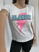 Remera blanca de algodón con estampado frontal de la palabra "Blondie" en letras celestes con borde negro y un rayo rosa.