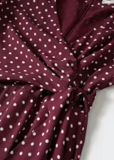 Mono largo color borgoña con estampado de lunares blancos, escote en V cruzado, mangas largas acampanadas, nudo en la cintura y forro interior.