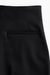 Pantalón palazzo negro de tiro alto con elástico oculto en la cintura, cierre lateral oculto y pinzas que realzan la figura. Modelo de corte holgado con bolsillos al bies, bolsillos decorativos atrás y piernas tres cuartos con raya adelante y atrás.