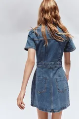 Vestido corto de denim azul, con cuello solapa, escote en pico, manga corta, bolsillos delanteros y cierre frontal con botones metálicos.