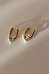 Aros tipo argolla dorados con dije colgante en forma de corazón de cerámica blanca.