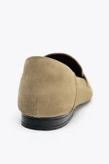 Zapato mocasín color beige de serraje con detalle de tira en la parte delantera y acabado en punta redonda.
