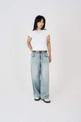 Pantalón de jean celeste de corte amplio, tiro bajo y cierre frontal con cremallera. Incluye cinturón negro con tachas plateadas.