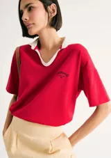 Camiseta roja de corte holgado con cuello polo blanco y logo estampado en el pecho.