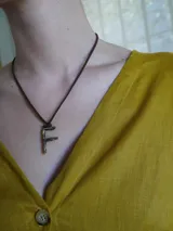 Gargantilla marrón de cuero con dije de bronce en forma de letra M.