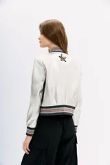 Campera bomber de cuero ovino color plateado, con cuello, puños y ruedo de ribb metalizado. Presenta apliques de parches bordados con lentejuelas y mostacillas.