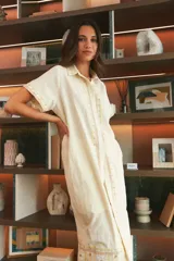 Vestido largo de lino en color celeste, con cuello camisero, manga corta y cierre frontal con botones. Presenta bordados decorativos en contraste en la pechera y en el ruedo.