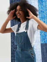 Jumper largo de denim azul con breteles regulables, bolsillos frontales y corte recto.