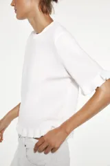 Top blanco de punto liso con cuello redondo y manga corta. Detalle de volantes en mangas y ruedo.