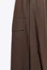 Vestido midi marrón de escote asimétrico con un hombro descubierto y una manga larga. La falda es amplia con bolsillos laterales y bajo tipo globo.