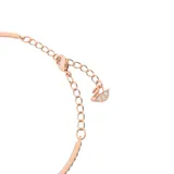 Pulsera de metal con baño en tono oro rosa, estilo brazalete abierto. Presenta un diseño central con una piedra redonda brillante suspendida dentro de una estructura ovalada. Un lado del brazalete está adornado con una hilera de cristales engastados.