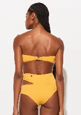 Bikini amarillo mostaza de dos piezas marca Triya. El corpiño es strapless y la bombacha es de tiro alto con aberturas laterales unidas por argollas con estampado floral.