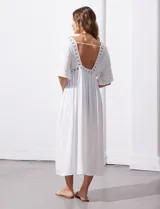 Kaftan blanco largo con mangas cortas y abertura central. Presenta apliques de puntilla en el escote, cintura y ruedo. Se ata en la cintura con un lazo.