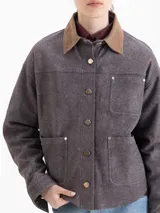 Chaqueta de cuero ovino color gris con terminación símil denim, de espíritu utilitario y moderno. Tiene bolsillos plaqué sobre el lado izquierdo y en cada lateral. El acceso es mediante broches metálicos. El cuello es de gamuza color tostado a contratono.