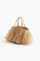 Bolso de mano tipo shopper confeccionado en paja de papel color natural con efecto desflecado. Tiene dos asas trenzadas y no está forrado.