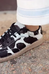 Zapatillas bajas con estampado de vaca en blanco y negro, cordones negros y suela color caramelo.