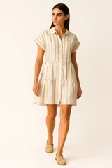 Vestido corto con cuello camisero, de corte holgado y mangas cortas. Presenta un diseño a rayas verticales en tonos beige y blanco, con volados en la falda y cierre frontal con botones.