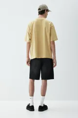 Remera color mostaza de algodón de peso medio, corte oversized, con cuello redondo ribeteado, hombros caídos y bajo recto.