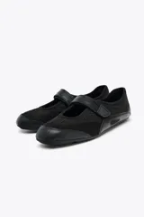 Zapato tipo bailarina color negro, con capellada de rejilla y cierre con tira de velcro.