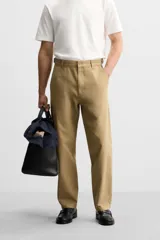 Pantalón chino color beige de corte recto, con cintura ajustable con cordón interior y trabillas laterales. Tiene bolsillos frontales y traseros de vivo.