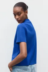 Chaqueta de punto azul con cuello solapa y manga corta. Tiene bolsillos delanteros de parche y cierre frontal con botones grandes con abalorios.