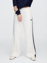 Pantalón deportivo azul marino de corte recto, con cintura elástica, bolsillos laterales y logo de Gap bordado en blanco. Presenta una franja blanca vertical en los laterales.