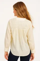Camisa color crema de algodón con cuello a la base, corte holgado, cierre frontal con botones y mangas largas con puños abotonados.