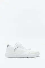 Zapatilla urbana blanca de mujer, con silueta moderna y líneas limpias. Presenta detalles en poliuretano liso y un panel plateado en el talón. La suela es de perfil recto y firme.