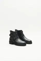 Bota de cuero negra con caña media, tiras cruzadas con hebillas y remaches metálicos, laterales matelaseados y cierre lateral interno.