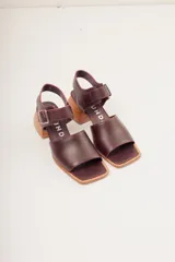 Sandalias negras de cuero con diseño minimalista y taco ancho geométrico en tono madera. La capellada lisa aporta una estética depurada y moderna, mientras que la pulsera con hebilla metálica ajustable asegura un calce firme y confortable.