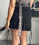 Minifalda negra ajustada al cuerpo con volado inferior y laterales ajustables con cordones.