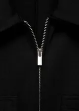 Mono largo negro de tejido fluido con diseño entallado, cuello polo, manga corta, cierre frontal con cremallera y dos bolsillos con cremallera en la parte frontal.