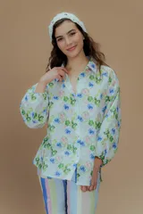 Camisa blanca con estampado de flores azules y hojas verdes, cuello clásico y mangas largas abullonadas.