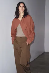 Pantalón marrón de tiro medio con trabillas en la cintura, bolsillos laterales, pinzas delanteras y bajo ajustable con trabilla y botón.