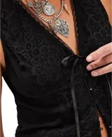 Chaleco negro de inspiración masculina, confeccionado en viscosa, con escote en V y cierre frontal con botones. La parte delantera presenta un diseño de encaje floral superpuesto sobre una base opaca, con un lazo de cinta de satén en el centro del escote.