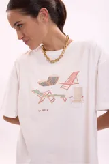 Remera blanca de algodón, corte oversize, con cuello redondo y manga corta. Presenta un estampado frontal con varias reposeras y hamacas de playa, y el texto "LA SIESTA".