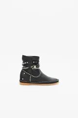 Bota de caña media color negro confeccionada en cuero, con suela de goma y terminaciones de costura manual y remaches metálicos. Presenta un cinto ornamental con tachas, cadenas y piezas en metal.