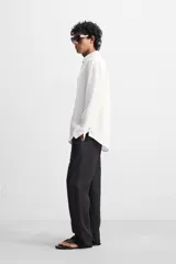 Camisa color arena de lino con cuello abotonado, manga larga con puños abotonados, corte regular y bajo con aberturas laterales.