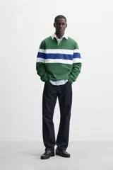 Polo de rugby verde con rayas horizontales azules y blancas, cuello blanco con solapa y cierre de botones, y mangas largas con puños acanalados.