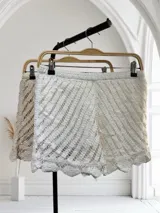 Short de tejido de punto calado color blanco, con forro interior. Presenta un patrón de rayas diagonales y un ruedo con borde festoneado.