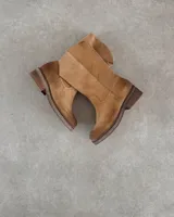 Botín corto de cuero vacuno color beige, estilo cowboy, con caña media y costuras decorativas en forma de onda en el empeine. Presenta un taco bajo y suela con pespunte visible.