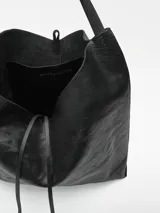 Bolso maxi hobo negro de piel bovina, con cantos al taglio, puntadas gruesas, un compartimento, cierre con nudo, asa de hombro y logo grabado.