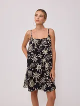 Vestido corto negro con estampado de palmeras, soles y estrellas en color crema. Diseño suelto con breteles finos y escote recto con lazo ajustable.