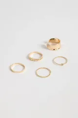 Set de anillos dorados con diferentes diseños, incluyendo un anillo ancho con textura, un anillo con corazones calados, un anillo liso, un anillo trenzado y un anillo con una pequeña piedra.